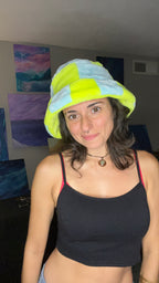 A woman wearing a fuzzy patchwork bucket hat in neon light blue and neon green